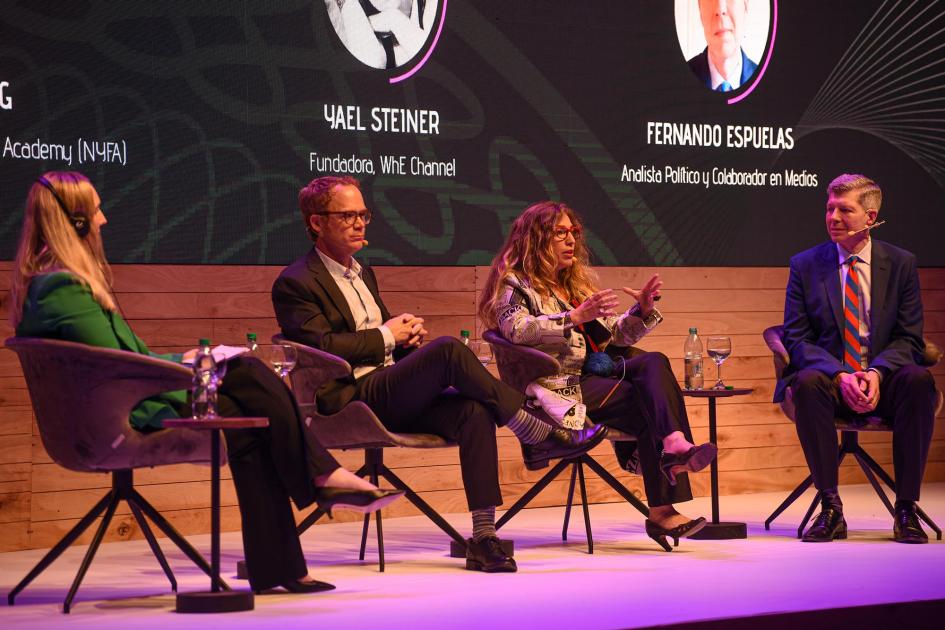 Dos hombres y dos mujeres dialogan sobre el escenario, sentados en sillas individuales