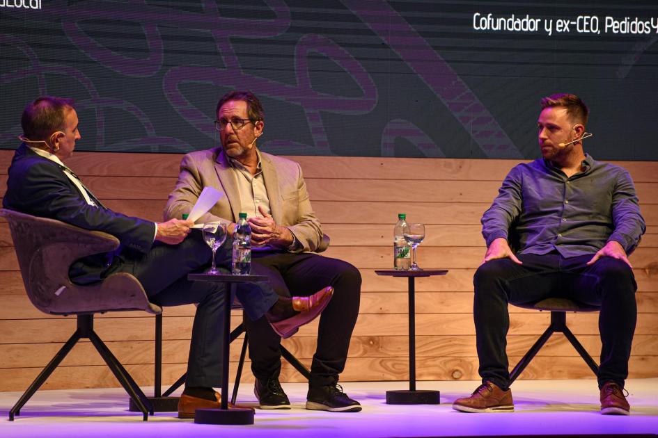Conversatorio sobre unicornios uruguayos Tres hombres dialogan sentados en sillas individuales, sobre el escenario