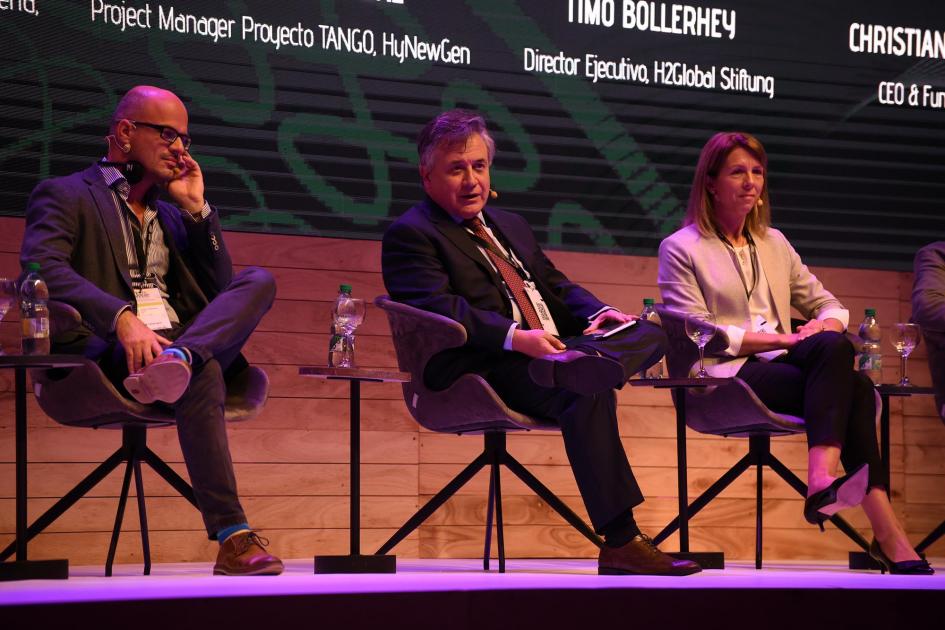 Ministro Omar Paganini Paganini habla en el escenario, junto a un hombre y una mujer; están sentados en sillas individuales