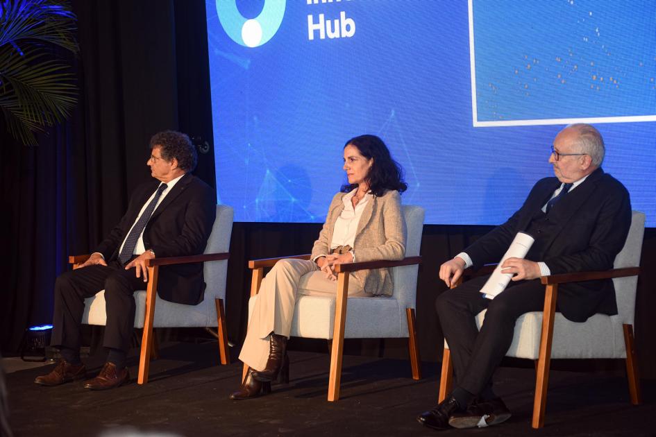 Panel de ministros Tres ministros, sentados; detrás, una gran pantalla con fondo azul