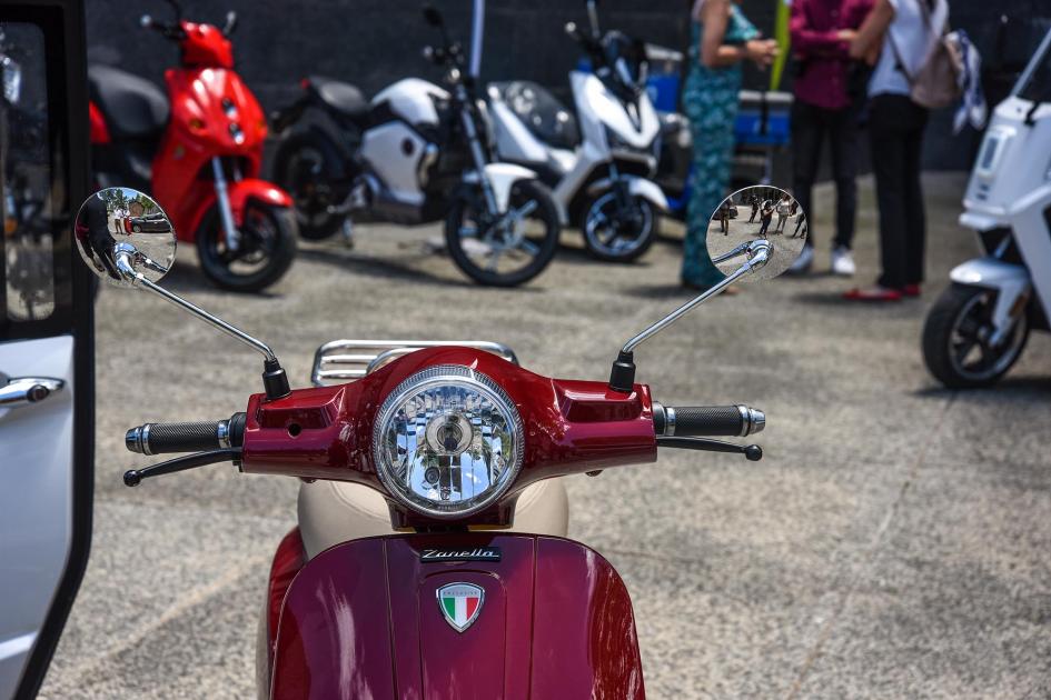 En primer plano, se ve una moto roja; al fondo, más motos de colores y un fragmento de un triciclo