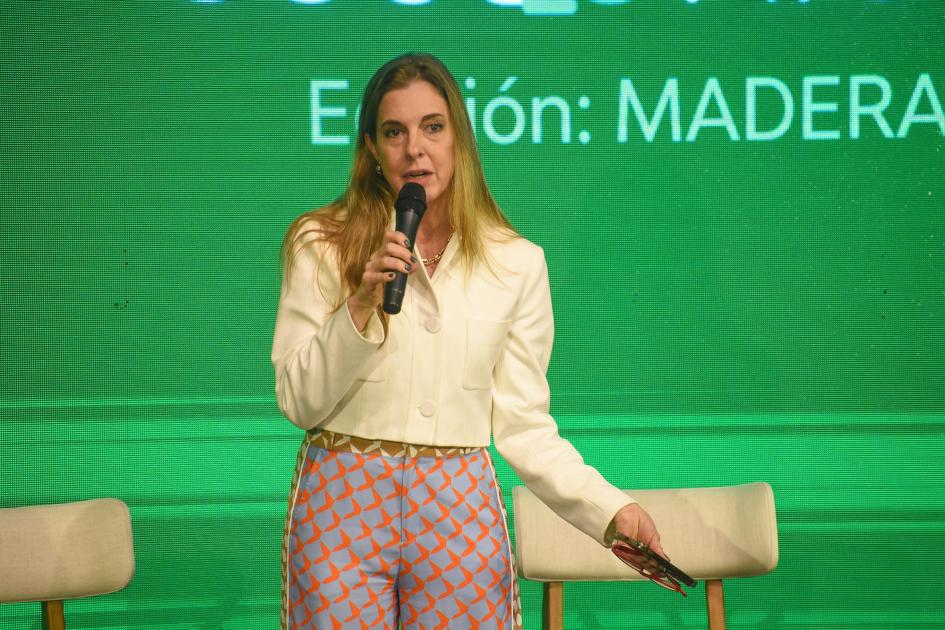 Carolina Moreira, representante de la Cámara de Comercio Uruguay-Países Nórdicos Moreira habla con un micrófono; detrás, pantalla verde con nombre del evento