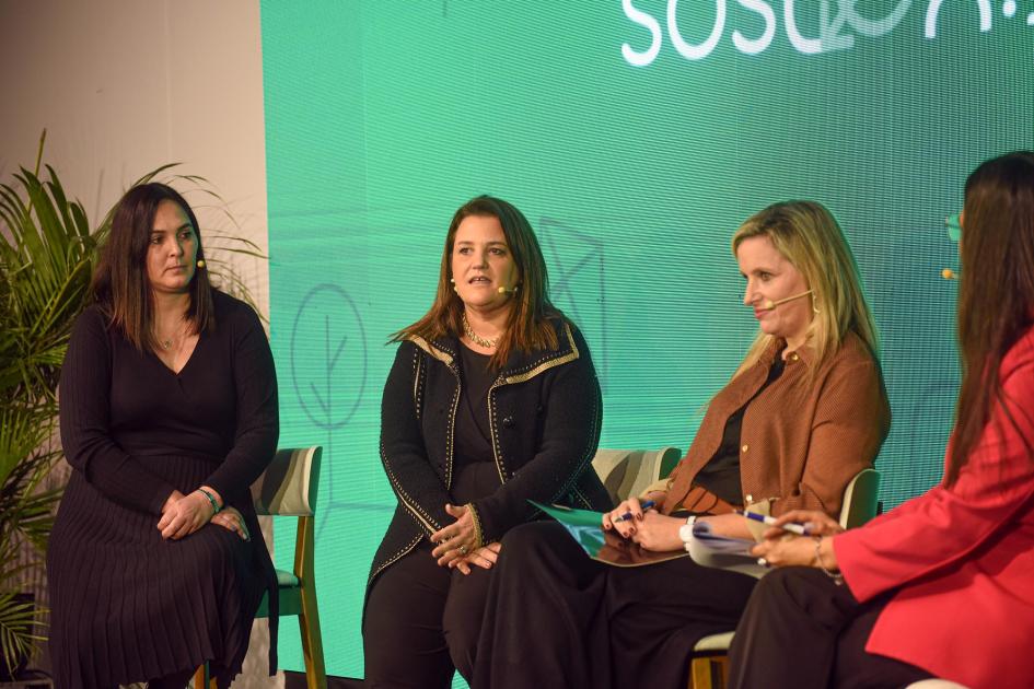 Segundo panel de intercambio del evento Cuatro mujeres dialogan, sentadas en sillas; detrás, pantalla con colores del evento