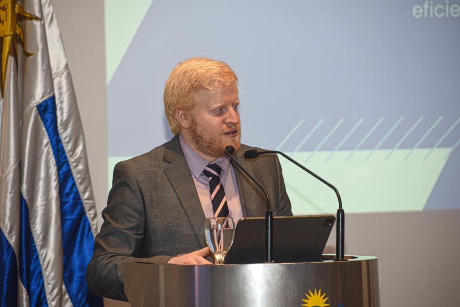 Director nacional de Energía, Christian Nieves Director Nieves habla en un atril; detrás, bandera uruguaya