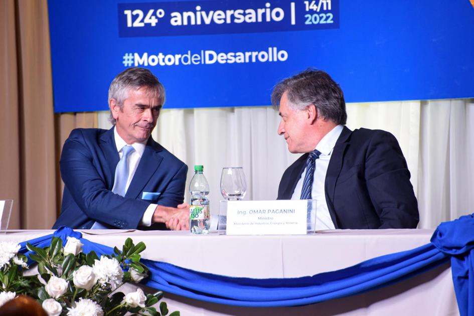 Omar Paganini y Alfredo Antía Paganini da la mano a Antía; detrás hay un banner azul del Día de la Industria