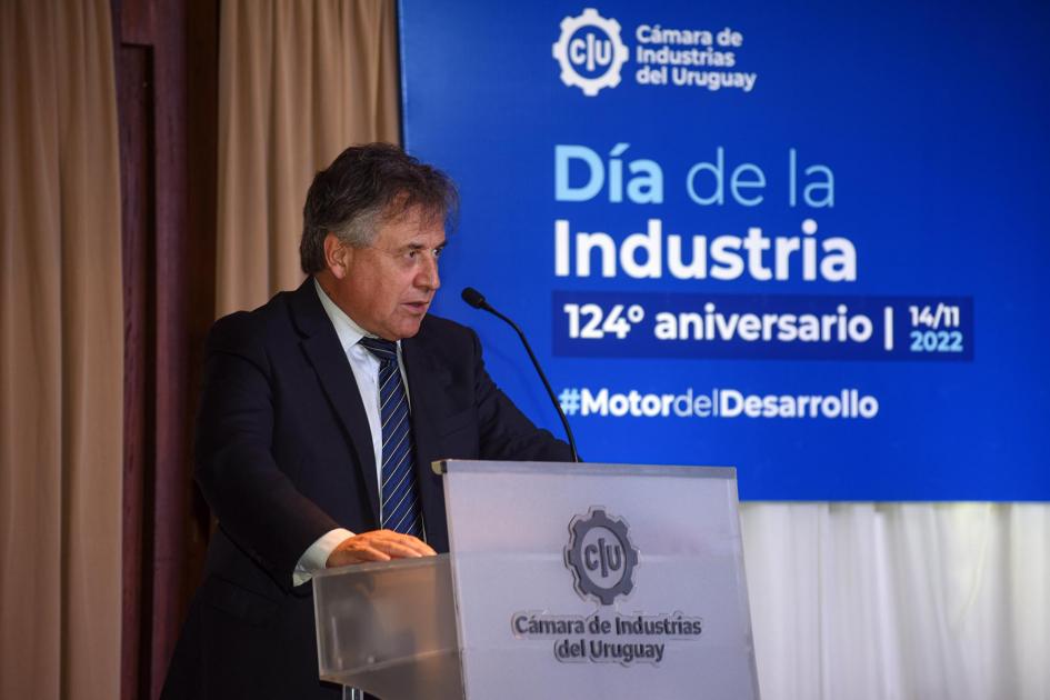Ministro Paganini habla desde un atril; a su lado, un banner azul del Día de la Industria