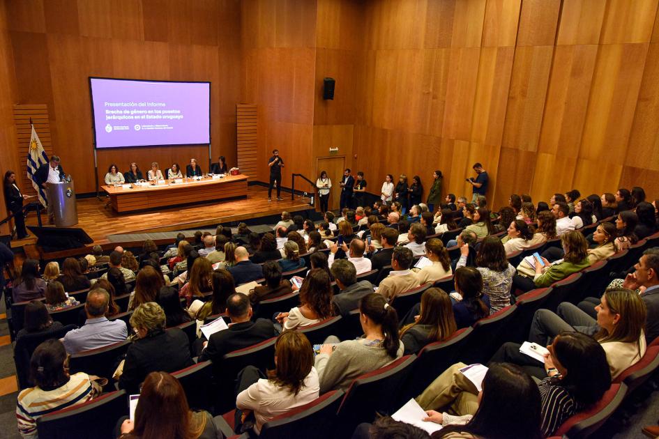 Autoridades y sociedad civil analizaron el informe de la ONSC Cerca, público sentado en anfiteatro; al fondo, mesa de autoridades, pantalla y bandera