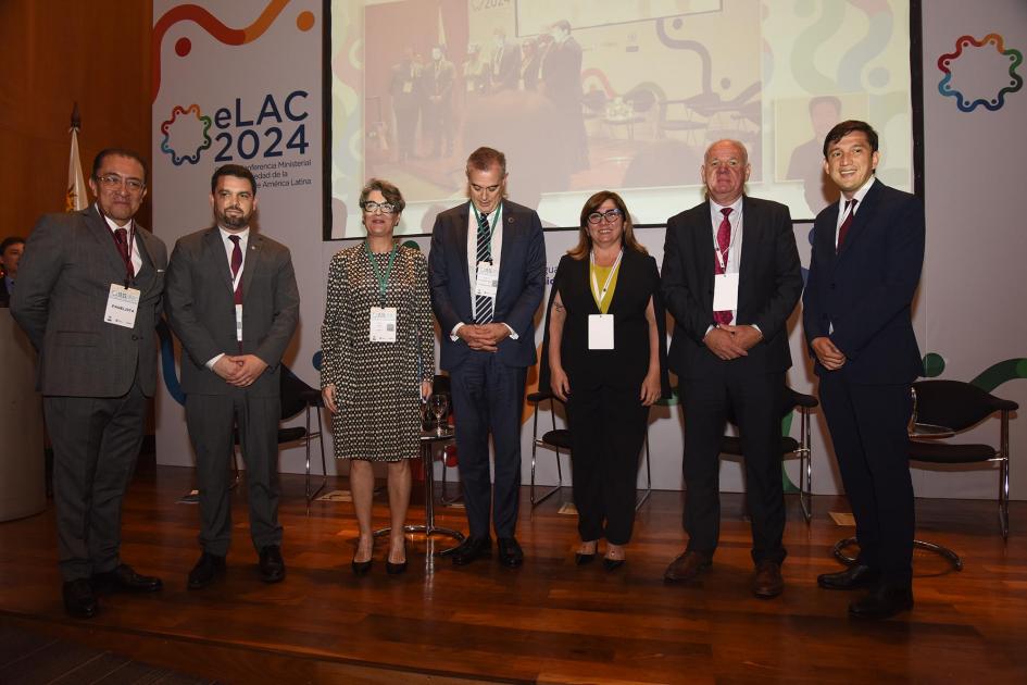 Panel en que participó el ministro interino Walter Verri Foto de los participantes del panel, de pie; detrás hay una pantalla