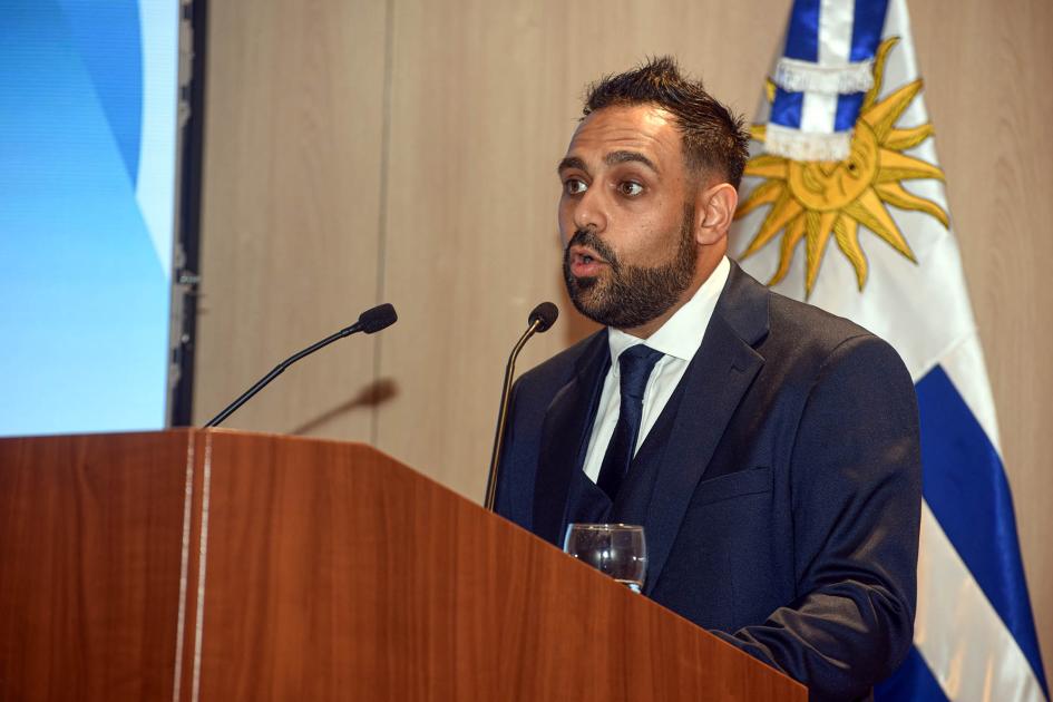 Presidente de AUDER, Diego Oroño Diego Oroño habla desde un atril; detrás, bandera uruguaya