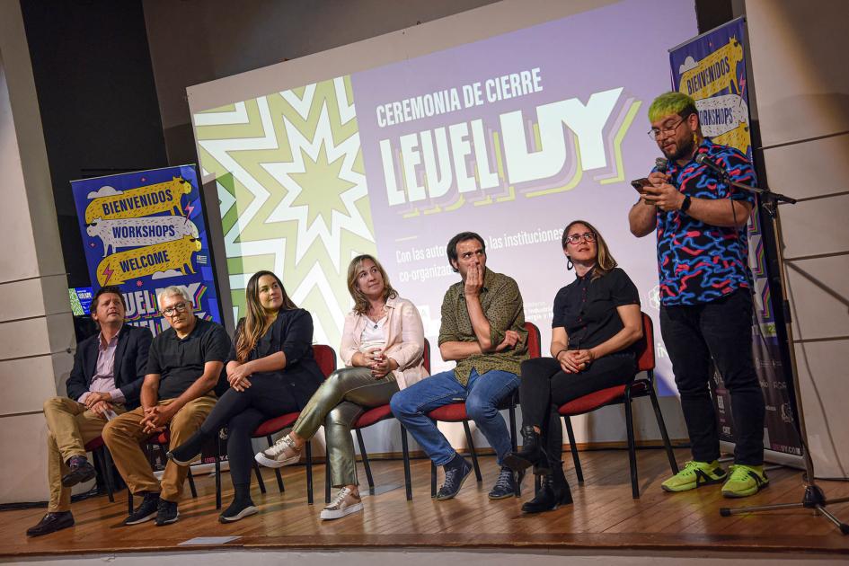 Personas sentadas en sillas en el panel de cierre; también hay un hombre de pie