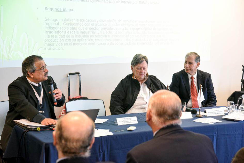 Director de Dinaten, Aníbal Abreu, habla en la mesa de expositores Mesa de expositores (tres hombres); frente a ellos, público