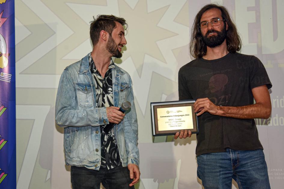 Representantes de TragicoMedia reciben su premio de la Convocatoria Videojuegos 2023 del MIEM Dos hombres; uno de ellos sostienen una placa