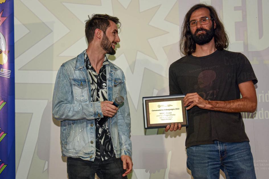 Dos hombres; uno de ellos sostienen una placa