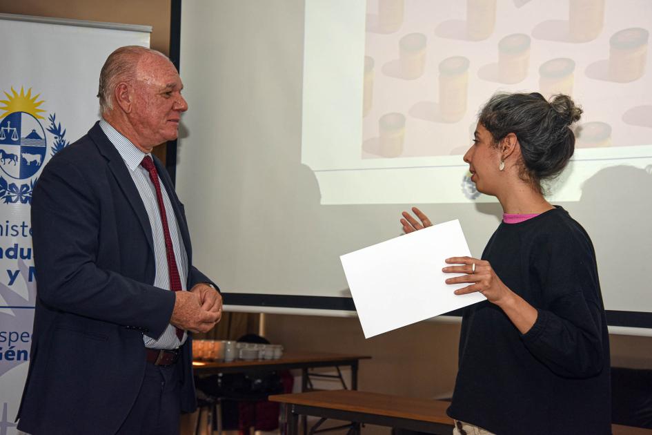 Maria de Castro, de Agni, dialoga con el subsecretario Walter Verri De Castro sostiene su diploma y dialoga con Verri; detrás, pantalla y banner