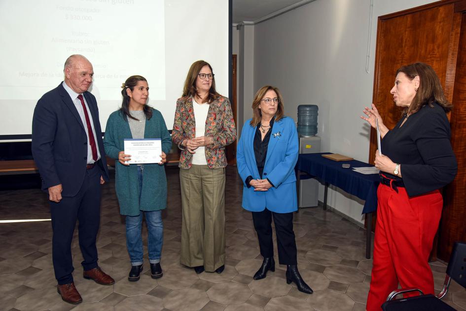 Vanessa Berrueta, de De la Casa Sin Gluten Vanessa Berrueta sostiene su diploma junto a autoridades, mientras habla Romero; detrás, pantalla