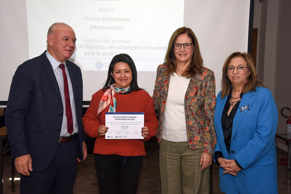 Daniela Rojas, de Paladeando Daniela Rojas sostiene el diploma junto a Facio, Verri y Bottero; detrás, pantalla