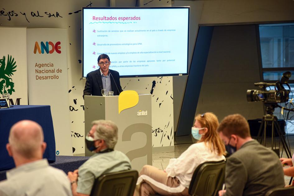 Durante el evento se ofrecieron detalles del programa Una persona habla en un atril; detrás se ve una pantalla y delante, el público