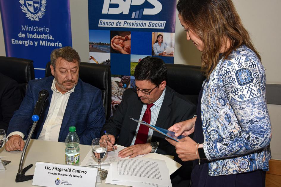 Firma del convenio Cantero firma junto a Cabrera; una mujer, de pie, le pasa los documentos