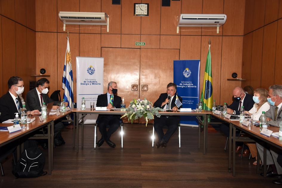 El ministro Paganini dio la bienvenida a la delegación brasileña Ministro Paganini habla en la mesa de trabajo; detrás, banderas nacionales y banners del MIEM
