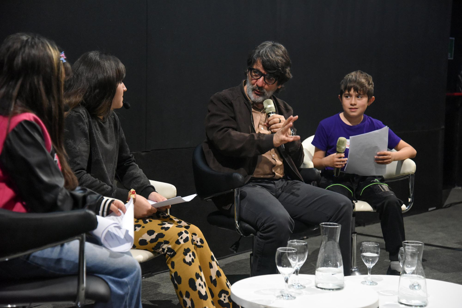 César Troncoso junto a niñas y niño César Troncoso junto a dos niñas y un niño, sentados.