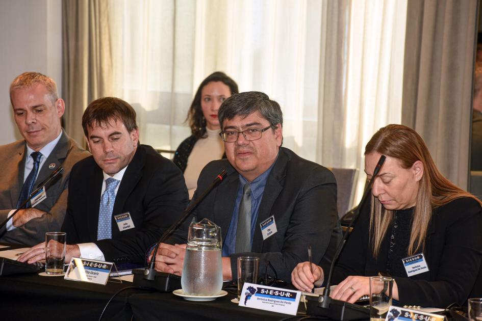 Representantes de los países integrantes de SIESUR Hombre habla junto a hombres y mujeres, sentados