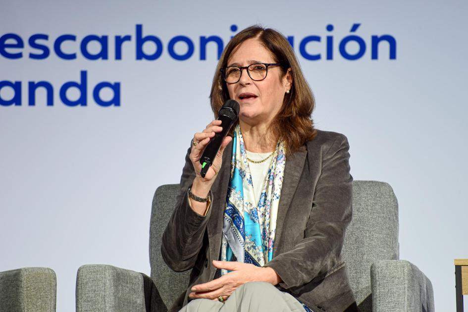 Ministra Elisa Facio Ministra Facio habla sentada, con un micrófono; detrás, banner del evento