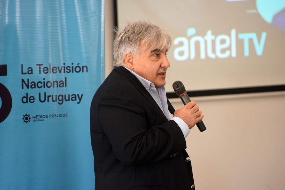 Alejandro Paz, presidente de Antel; detrás, banner de Canal 5 y pantalla con logo de Antel Paz habla con un micrófono; detrás, banner de Canal 5 y pantalla con logo de Antel