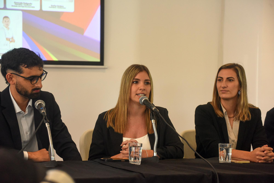 Presentación de parte del equipo periodístico Mujer periodista habla, sentada junto a un hombre y una mujer