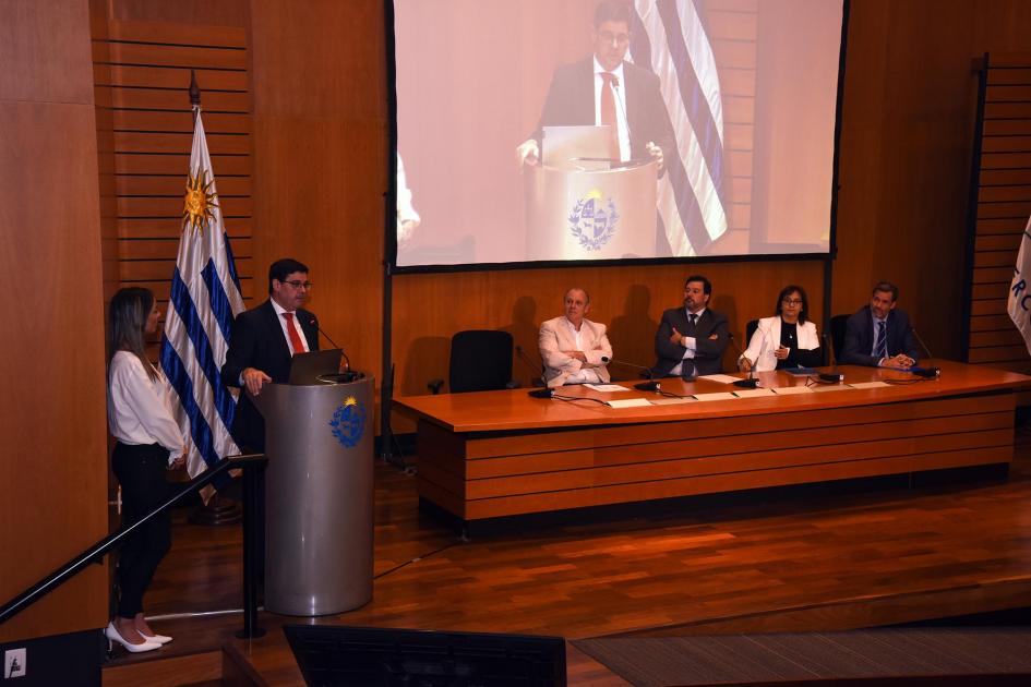 Director Cantero habla desde un atril, junto a la maestra de ceremonias y una bandera; al lado, mesa