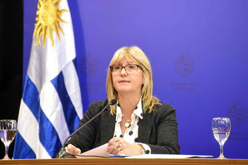 Ministra Cristina Lustemberg Lustemberg habla; detrás, bandera uruguaya