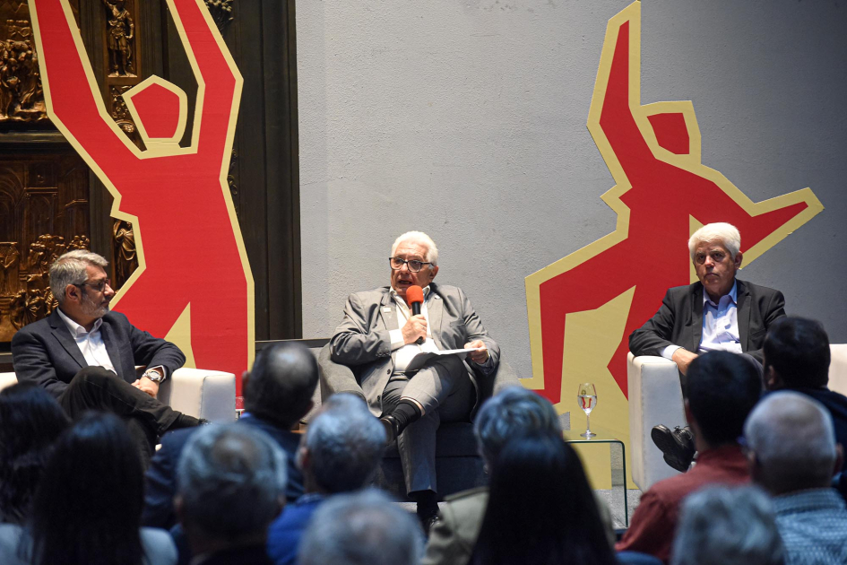 Montaño habla, sentado, junto a dos autoridades, y frente al público