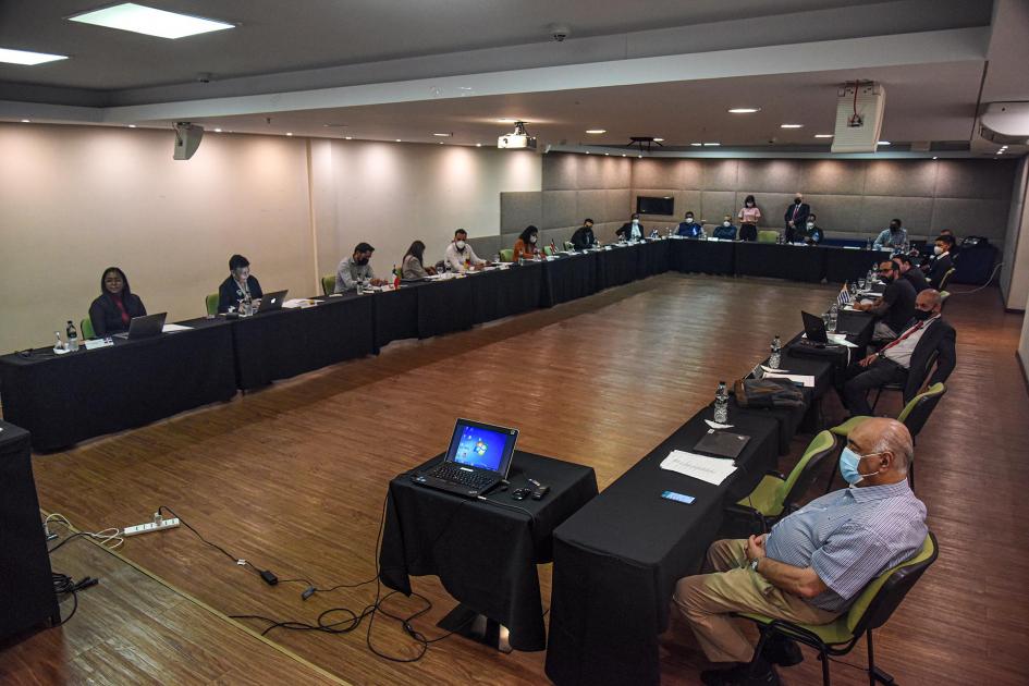 Participantes del evento, sentados en mesas en "u" y mirándose frente a frente