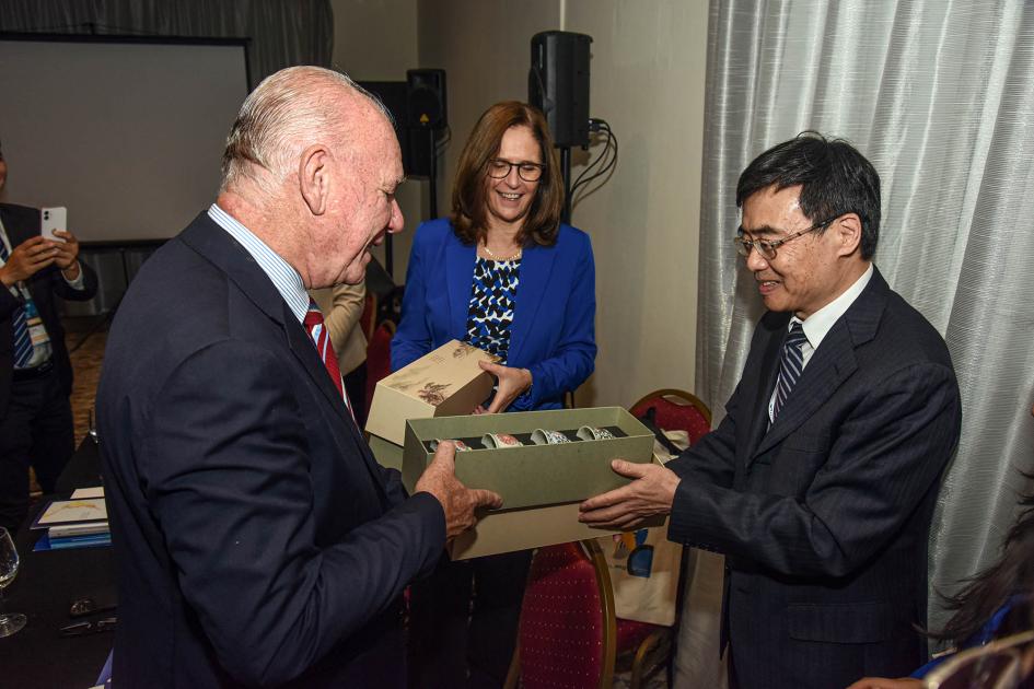 Verri recibe un regalo de un delegado chino (tazas en una caja), mientras la ministra Facio sonríe