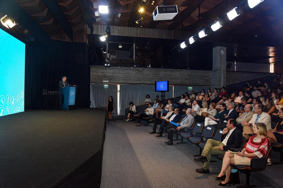 Ministro Omar Paganini Ministro Paganini habla desde un atril; junto a él, una gran pantalla; frente a él, el público