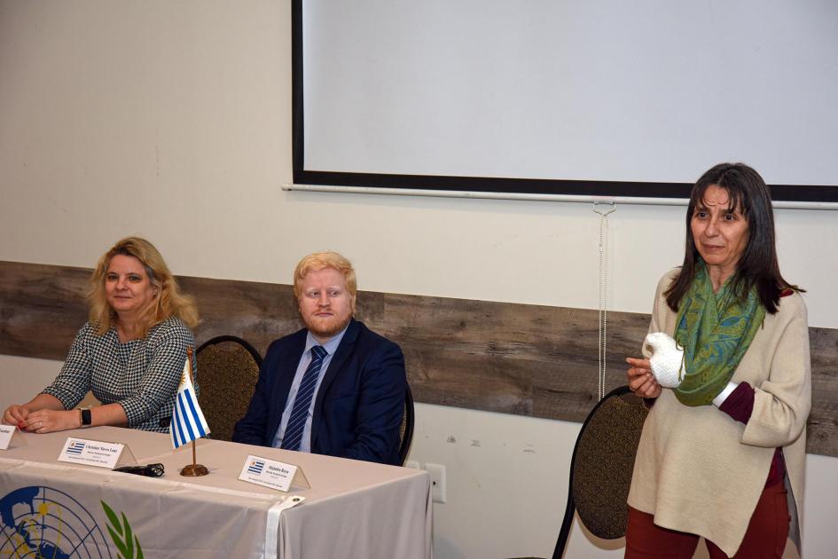 Gerente del Área Planificación, Estadísticas y Balance de la DNE, Alejandra Reyes Reyes habla, de pie; tiene la mano vendada; a su lado, Nieves y Bardellans, sentados