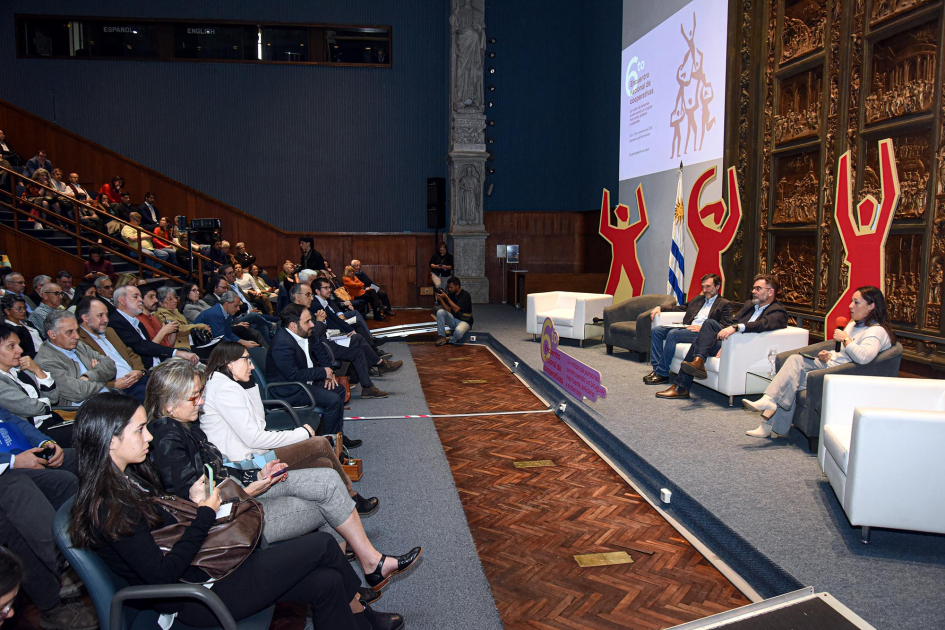 A la derecha, expositores y expositoras, sentados; frente a ellos, público