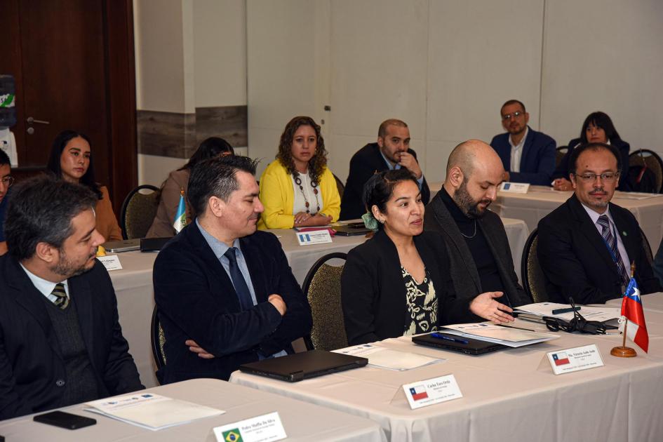 Participantes del taller Participantes del encuentro, sentados en dos mesas paralela y una, más chica, ubicada a su izquierda