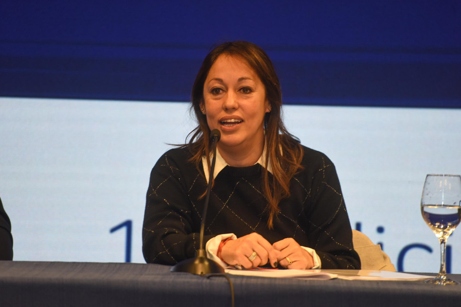 Cardona habla, sentada; detrás, pantalla