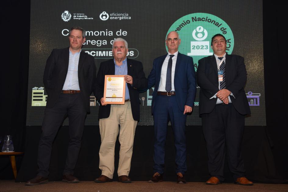 Representantes de la Intendencia Departamental de Florida Cuatro hombres; uno de ellos sostiene una placa; detrás, una pantalla