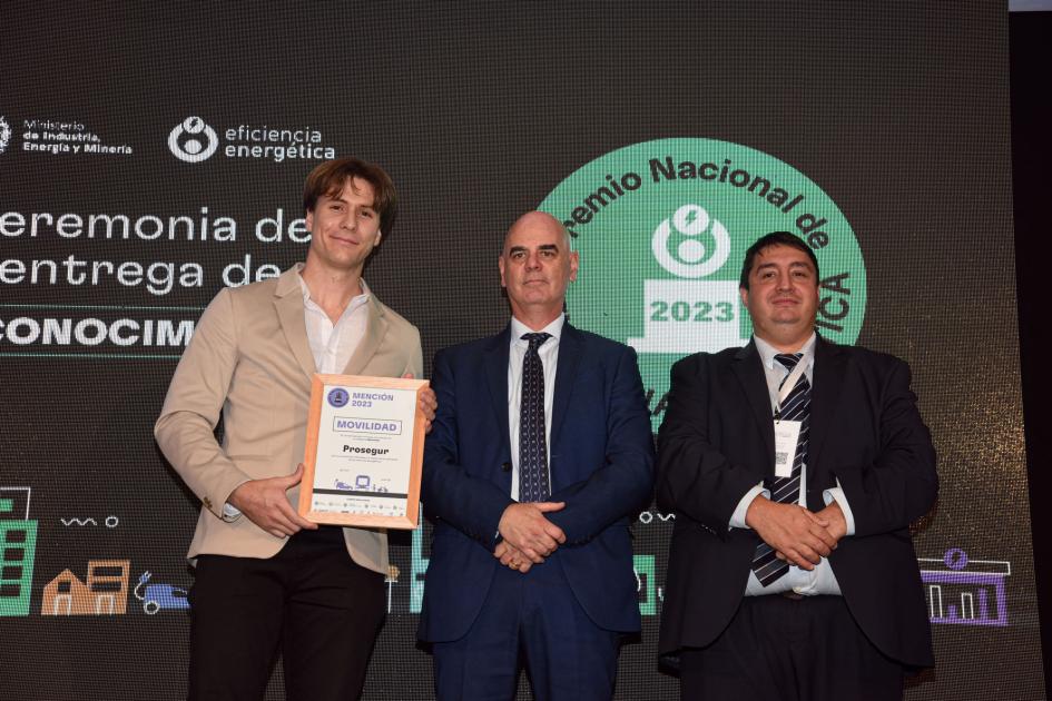Representantes de Prosegur Tres hombres; uno sostiene la placa; detrás, una pantalla