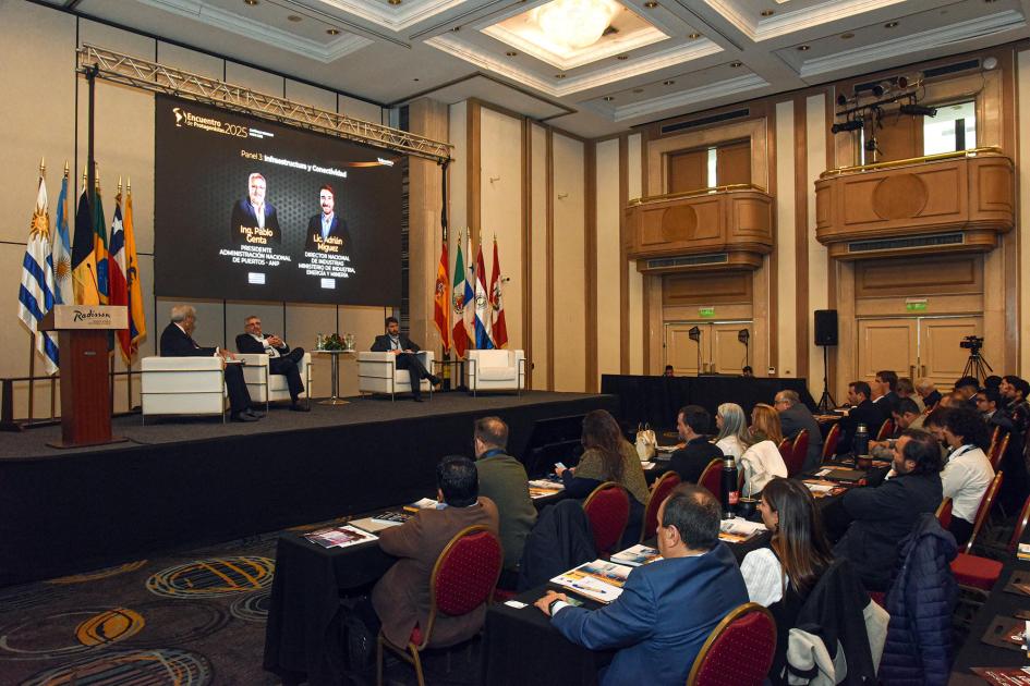 Público sentado, de espaldas; al fondo, autoridades del evento en el escenario. 