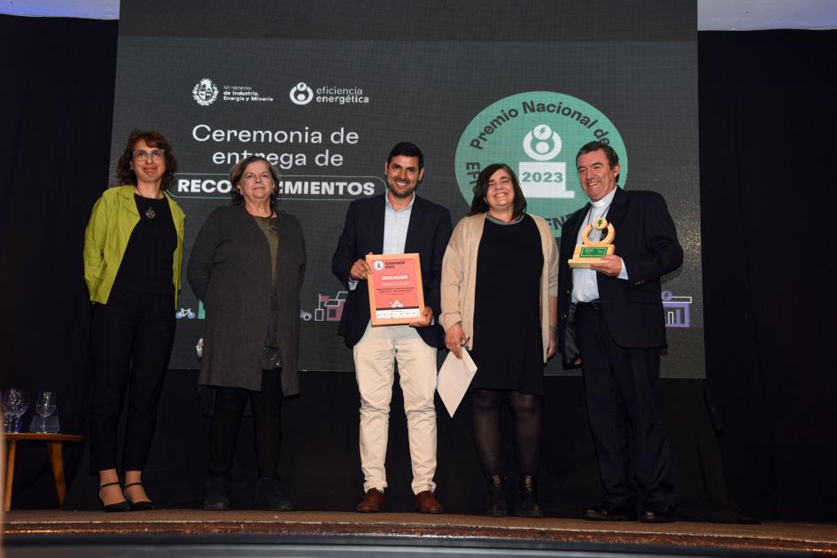 Representantes de la Especialización en vehículos híbridos y eléctricos de Talleres Don Bosco Tres mujeres y dos hombres; estos dos sostienen la placa y el premio; detrás, una pantalla