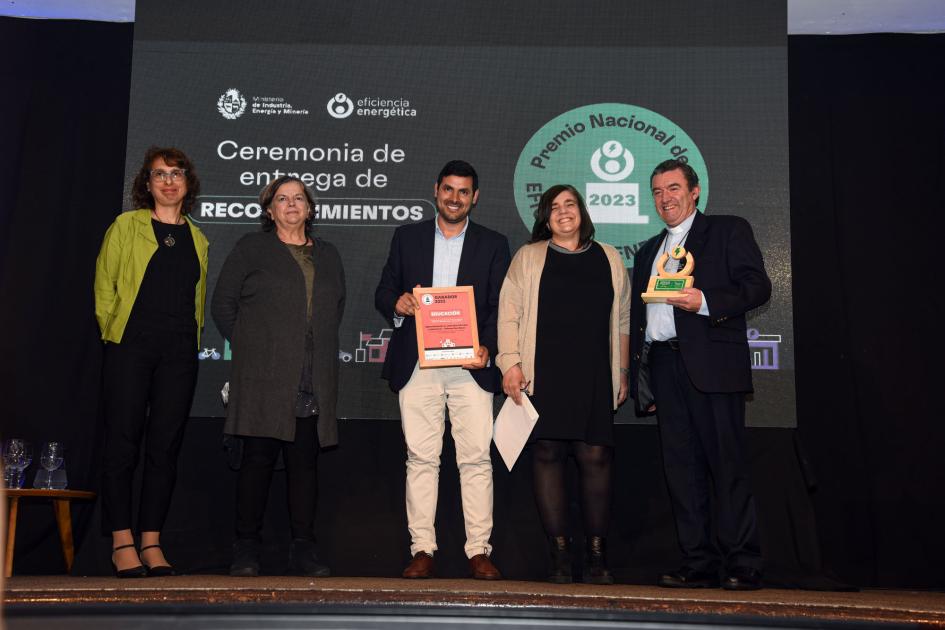 Tres mujeres y dos hombres; estos dos sostienen la placa y el premio; detrás, una pantalla