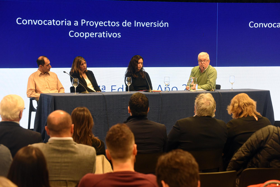 Al fondo, mesa con cooperativista y funcionario del MIEM; detrás, pantalla; más cerca, público
