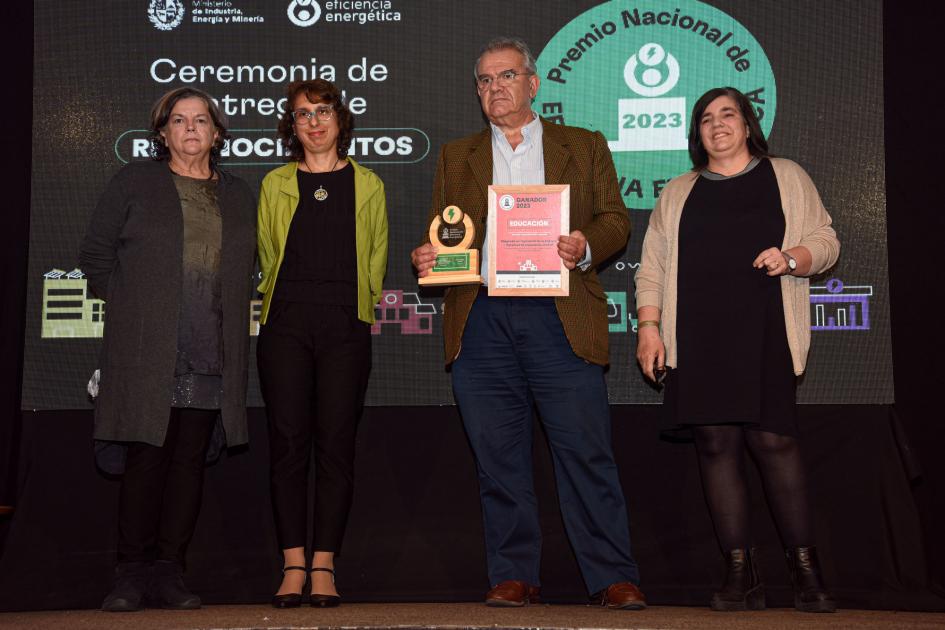 Tres mujeres y un hombre, que sostiene la placa y el premio; detrás, una pantalla