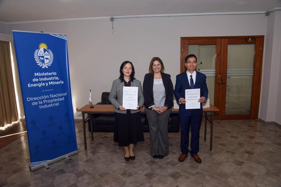Directora Marianela Delor y técnicos chinos Tres personas paradas junto a un banner institucional