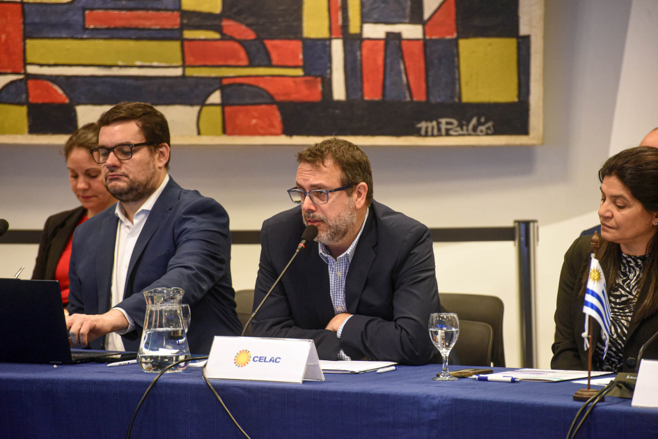 Director general para Asuntos Económicos Internacionales de Cancillería, Ricardo Baluga Baluga habla, sentado en una mesa junto a otras personas; detrás, mural