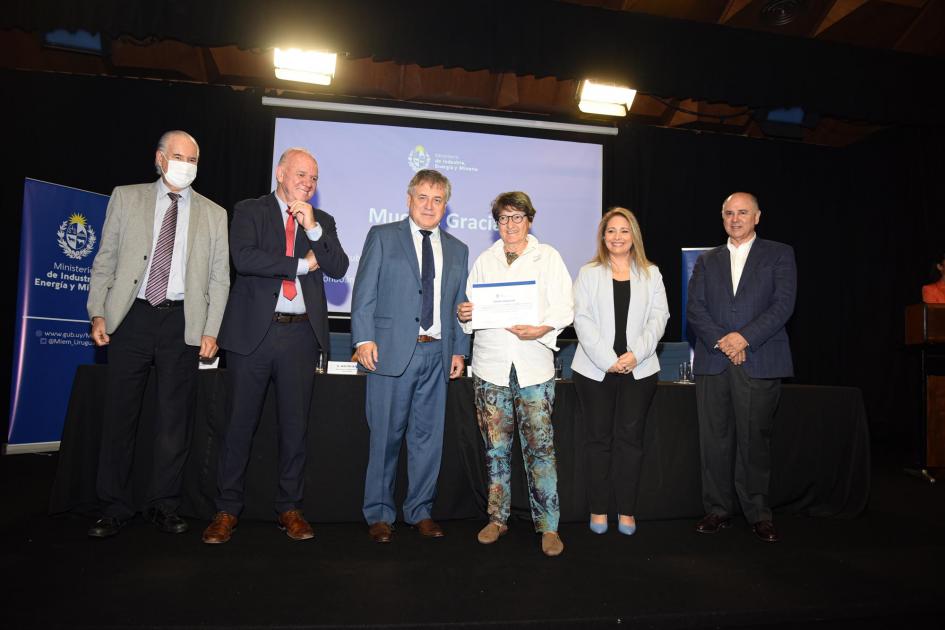 Certificado para Pique Roto Una mujer muestra su certificado junto a las autoridades; detrás, una pantalla azul