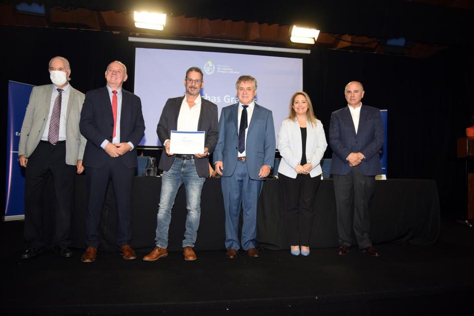 Delomar SA Un hombre muestra su certificado junto a las autoridades; detrás, una pantalla azul