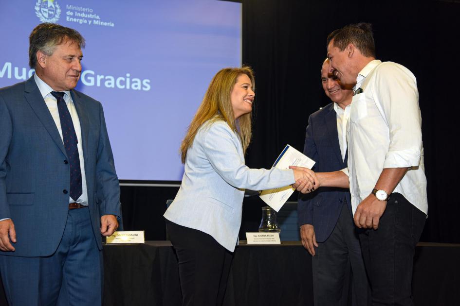 Un hombre saluda a la directora Pecoy al recibir su certificado; al lado de Pecoy, el ministro